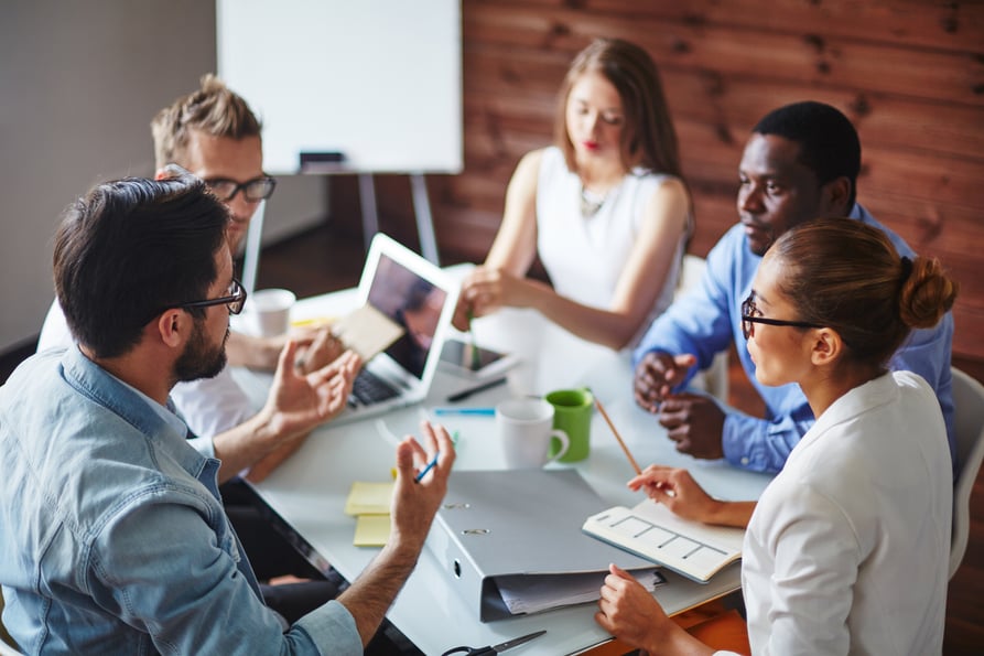 Employees sitting around a table in a meeting, able to focus on work because of auto attendant.