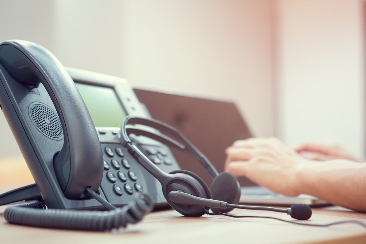 A headset leaning against a VoIP phone on a desk.