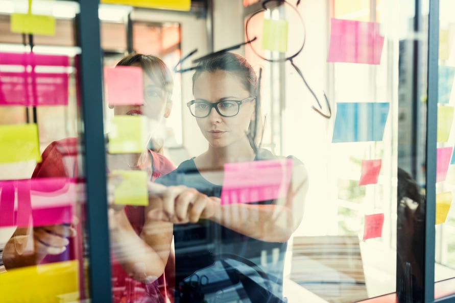 Two women working out a business plan on a whiteboard. 