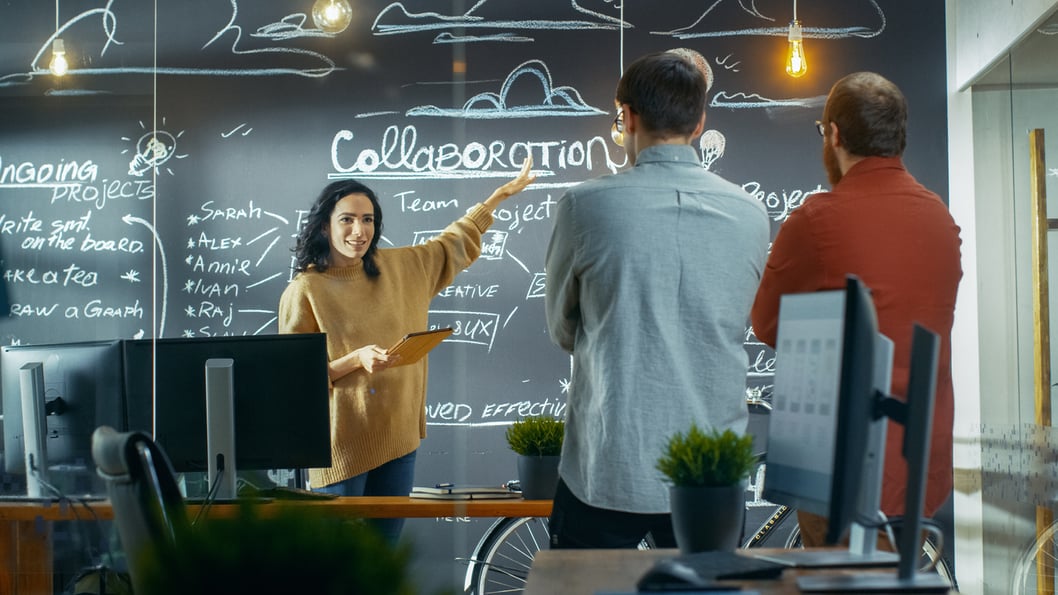 Three colleagues collaborating on a project using a chalkboard.