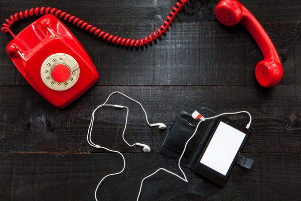 Red rotary phone sitting next to softphone with headphones.