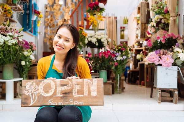 Business owner at a flower shop holding a sign with her business hours.