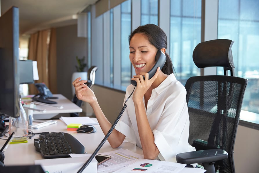 Businesswoman talking on a desk phone in an office.