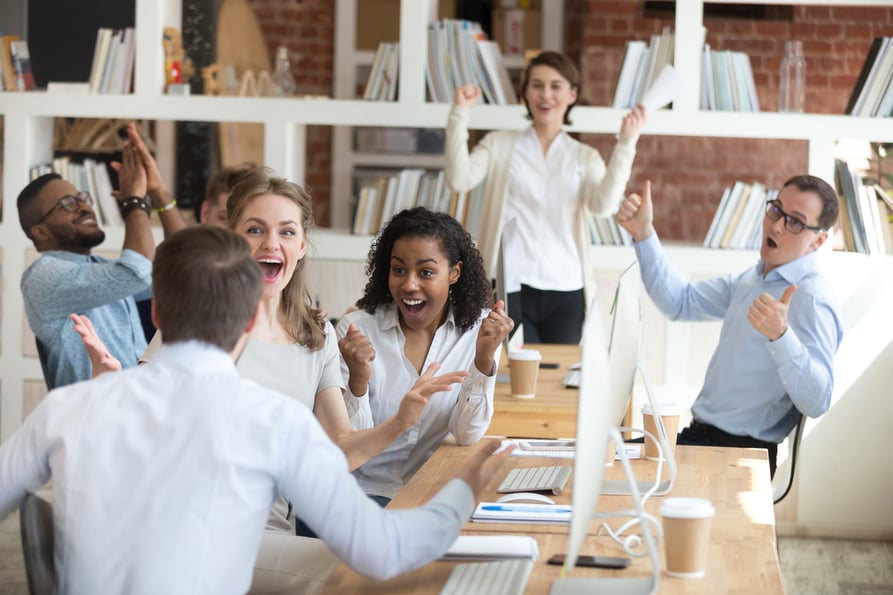 Group of business colleagues around a desk celebrating closing a deal.