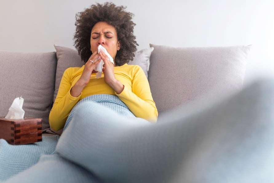 Sick woman on. couch sneezing into a tissue.