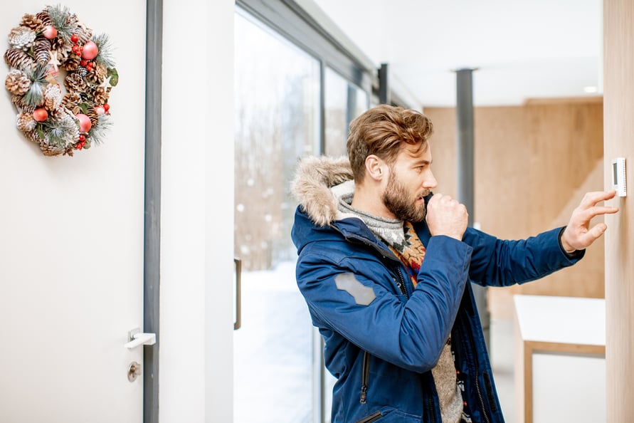 Man in fur parka adjusting wall thermostat.