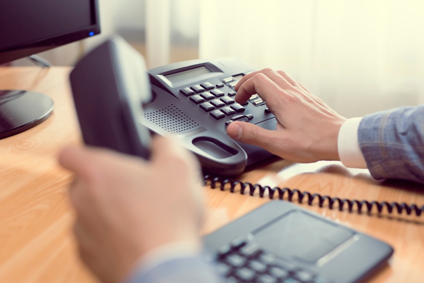 Person dialing a desk phone.