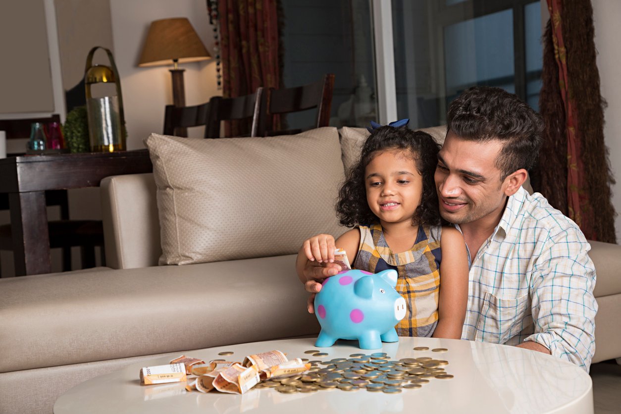 Father and daughter putting money in a piggy bank.