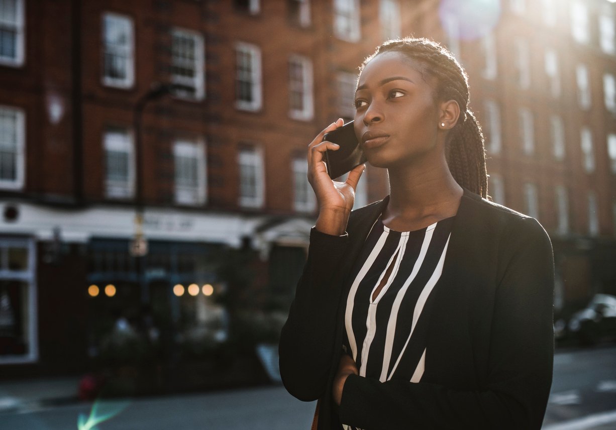 Woman on a city street waiting on hold on her cell phone.