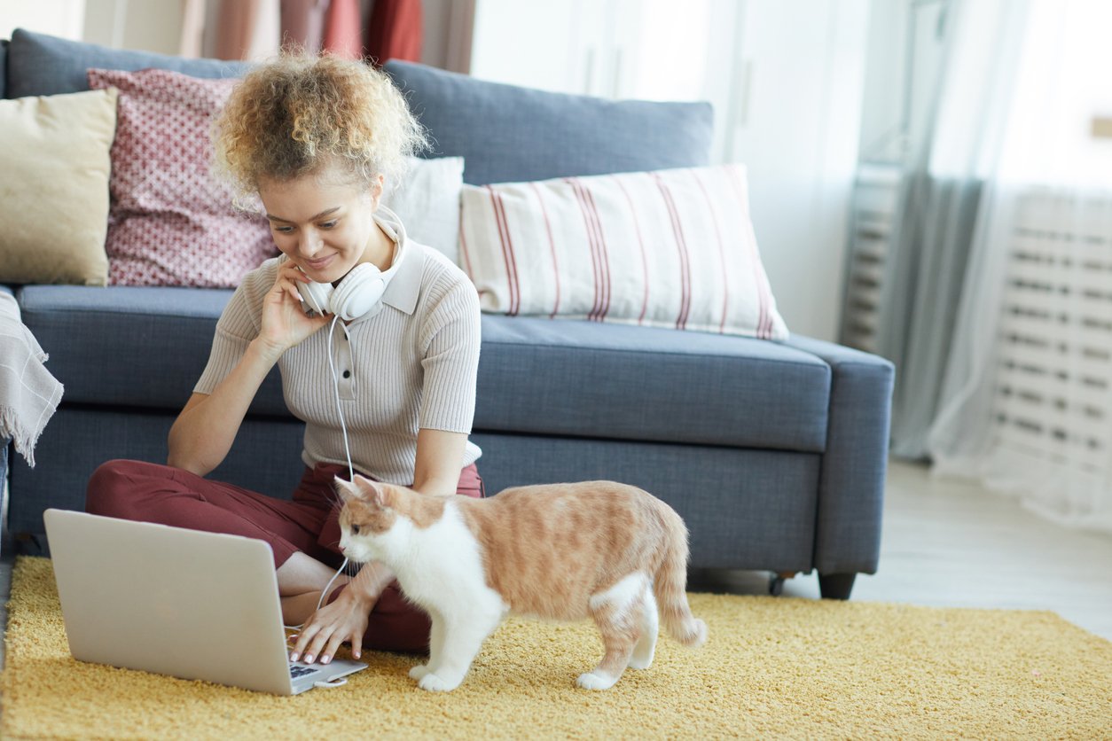 A young woman works comfortably from home with her cat nearby.