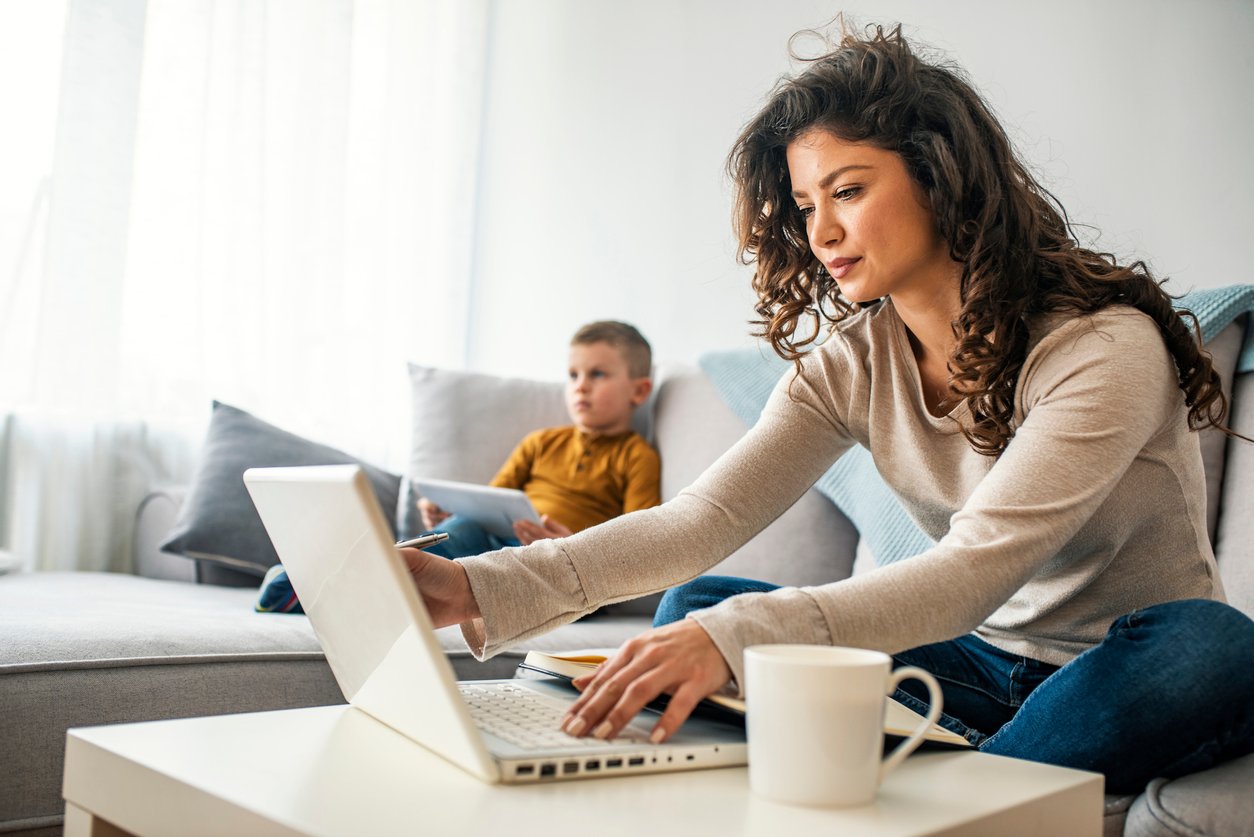 A mother works remotely with her son nearby.