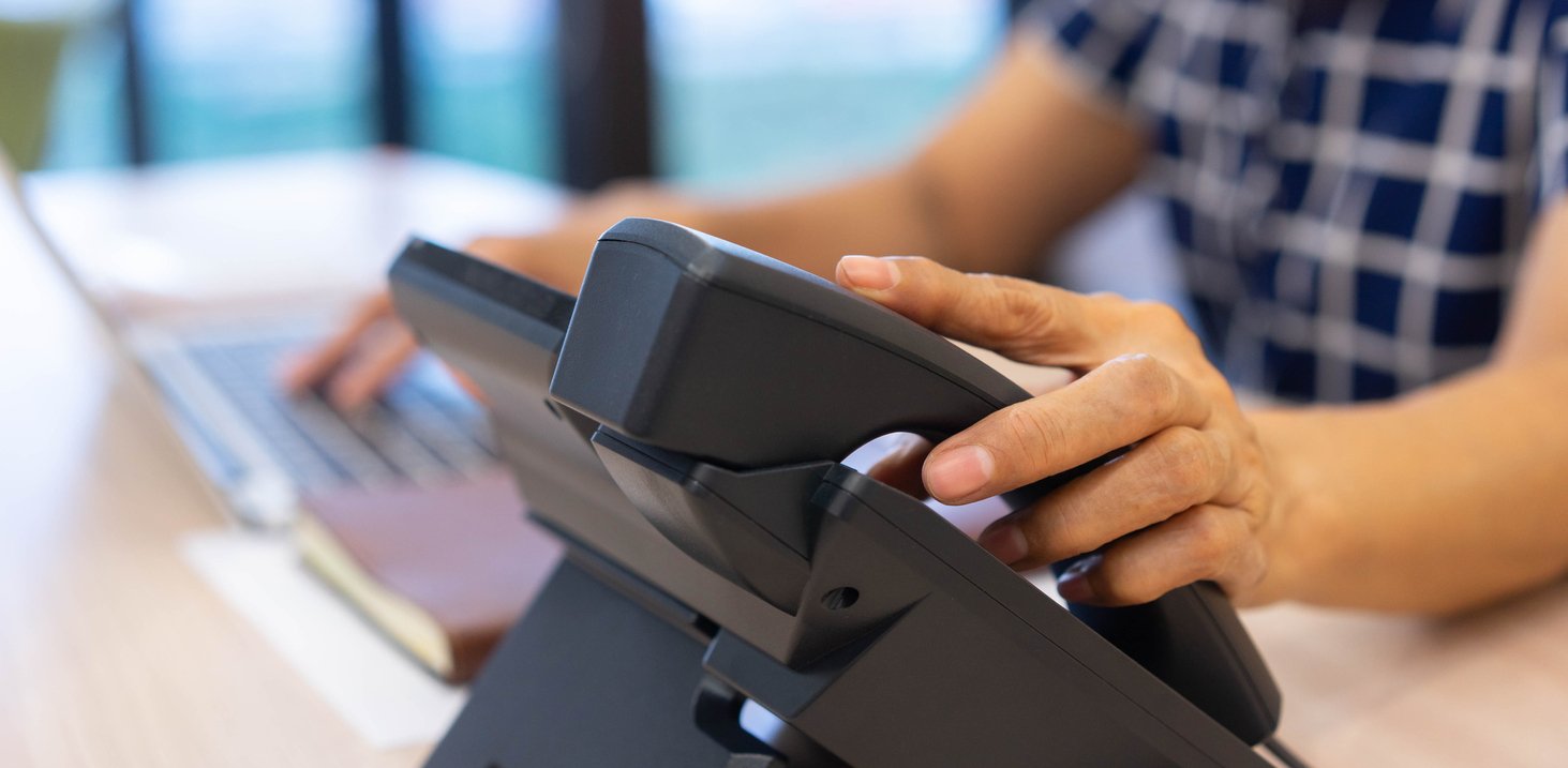 Person's hand on a desk phone.