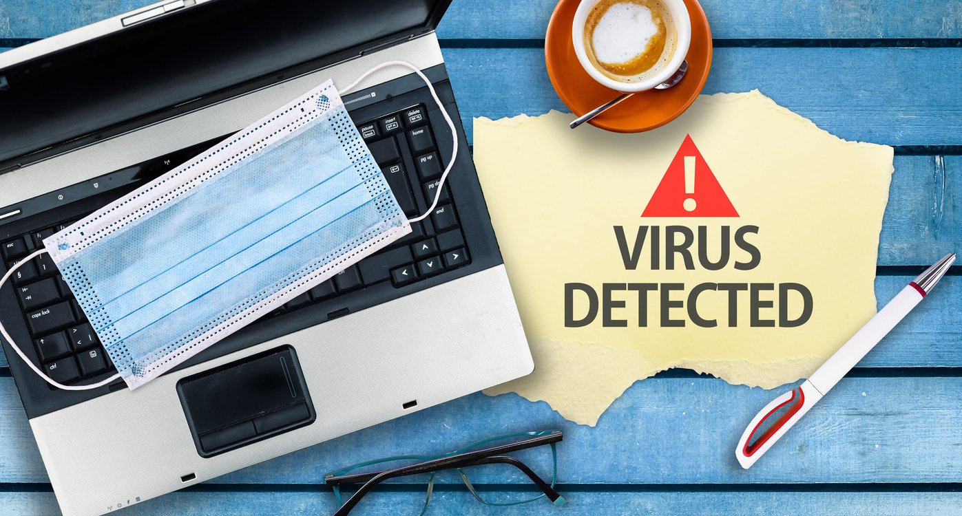 A sign saying Virus Detected next to a laptop with a surgical mask on the keyboard.