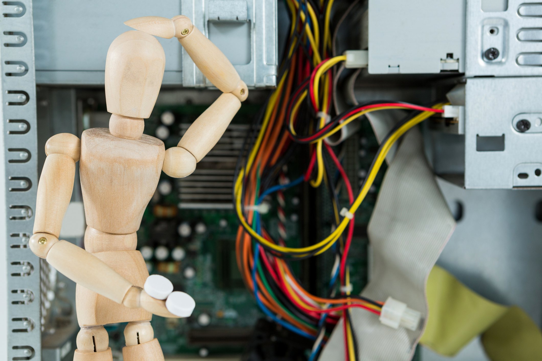 A toy human model posed scratching its head in front of IT wires.