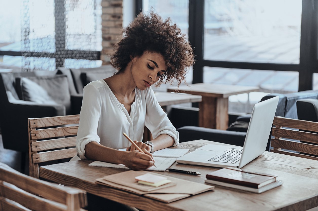 Woman takes notes while working on her laptop.