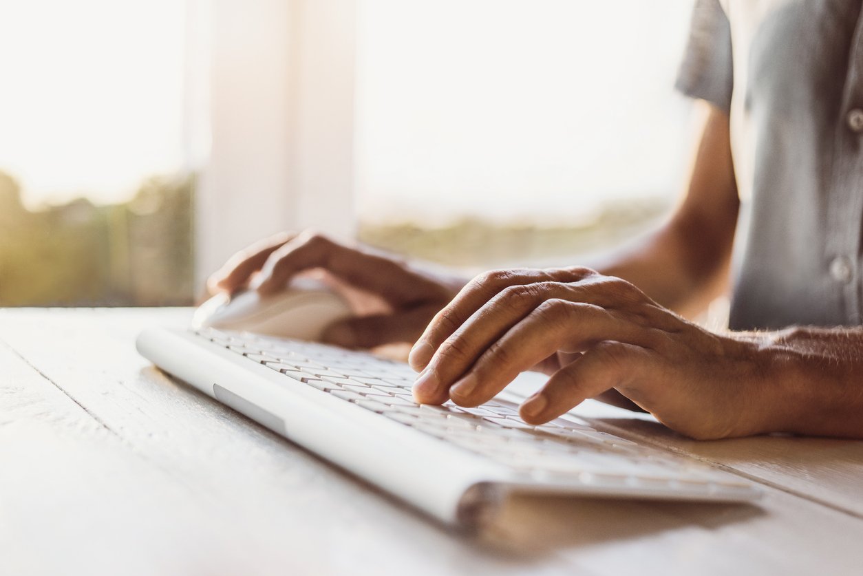 A person types on a bluetooth keyboard set far back from the computer out of the frame.