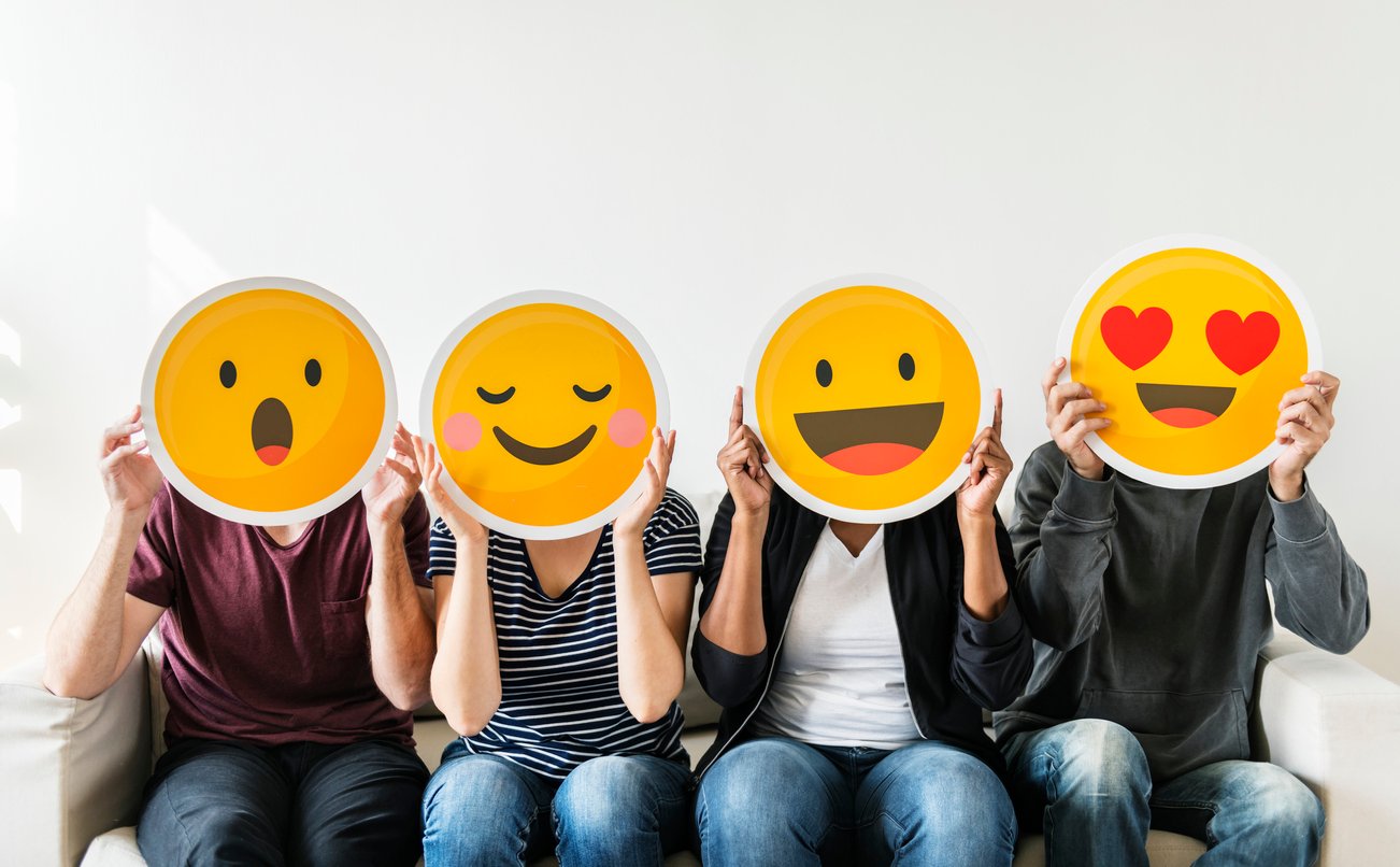 Group of individuals sitting in a row with emoji expression cutouts covering their faces.