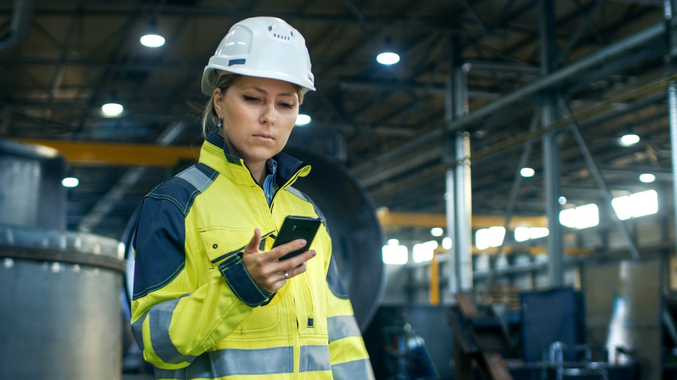 Woman at work in hard hat calling customer service on her cell phone.
