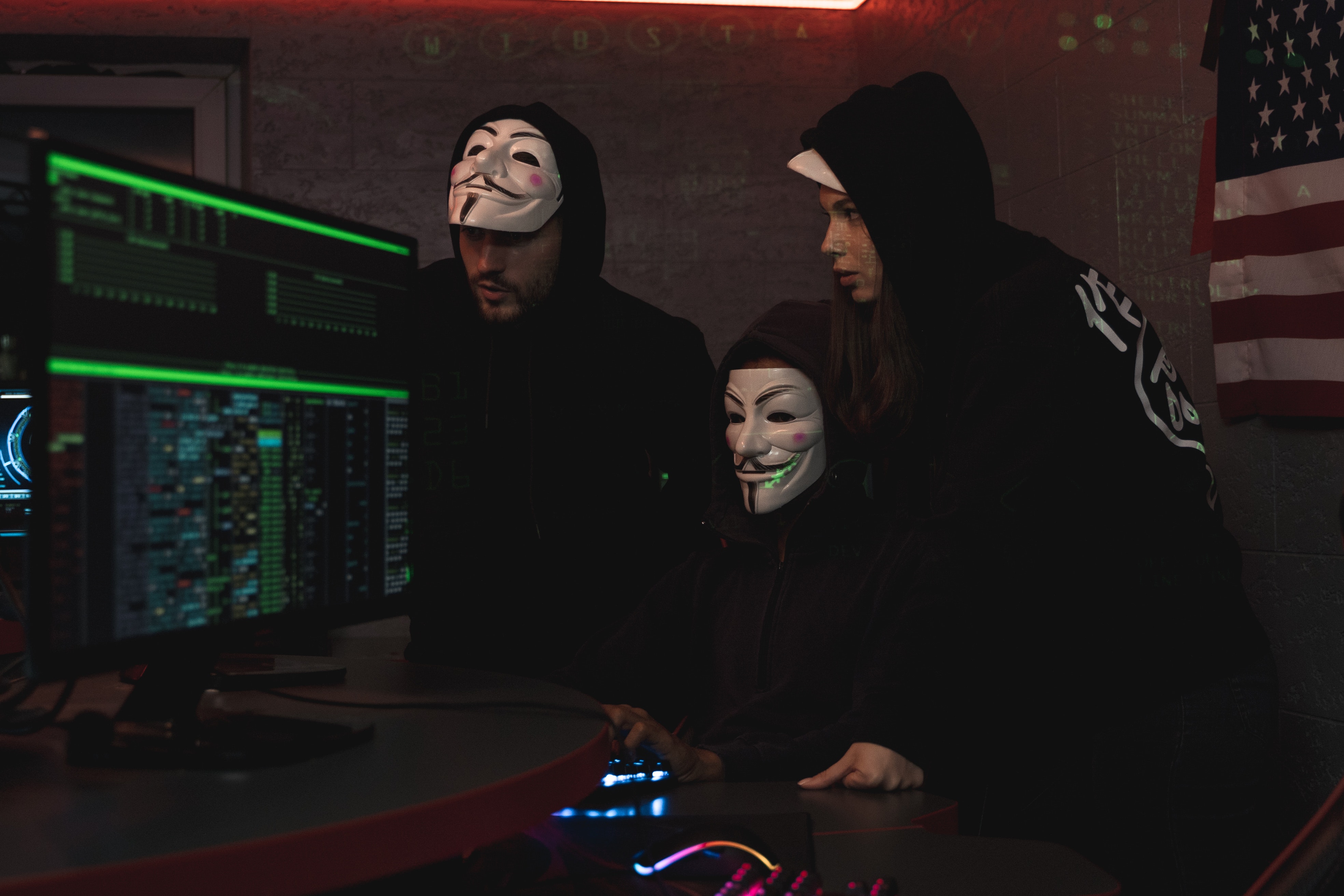 Hackers in V masks look at a monitor together.