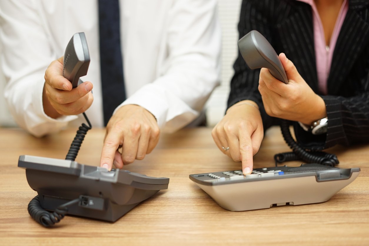 Two work colleagues configuring their VoIP desk phones.