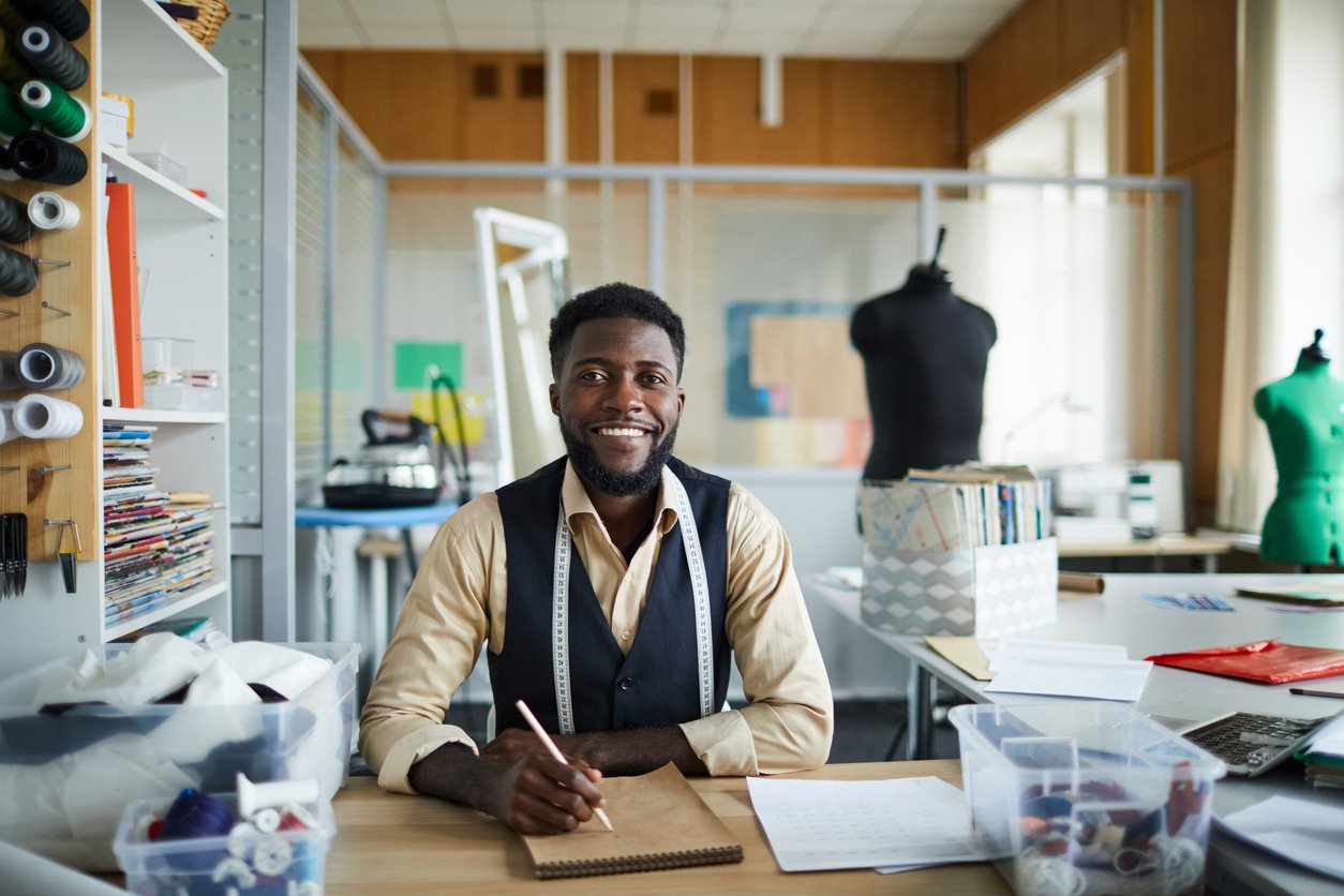 Tailor sitting at his business looking happy because he has a vanity phone number that's specific to his business.