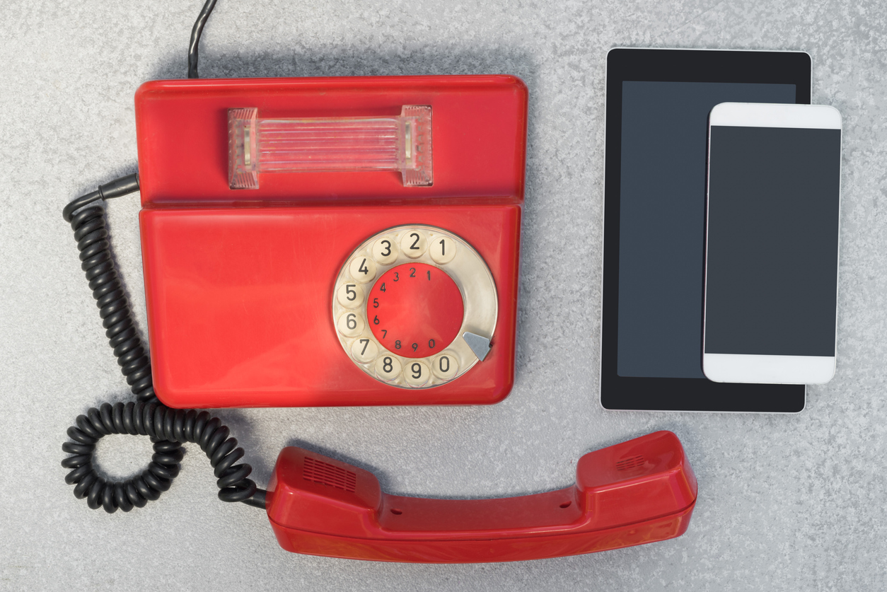 Old red rotary phone sitting next to a tablet and smartphone.