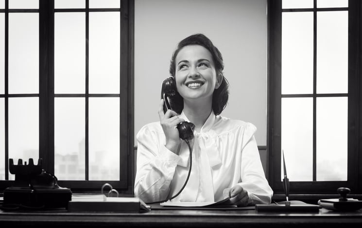 Black-and-white photo of a 20th-century receptionist using a rotary phone.